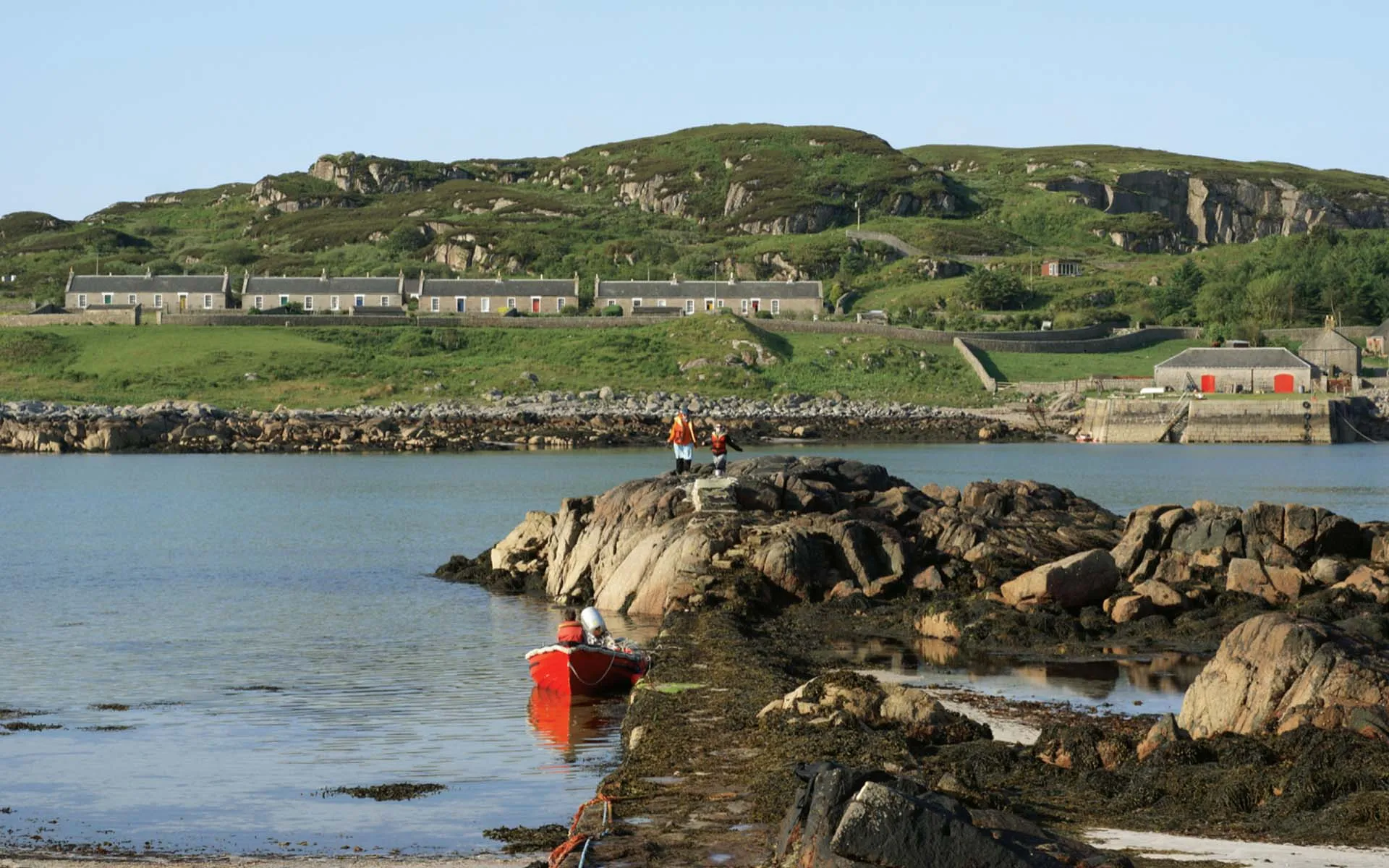 View across the water of the houses on the Isle of Erraid, rocks and seaweed in the foreground